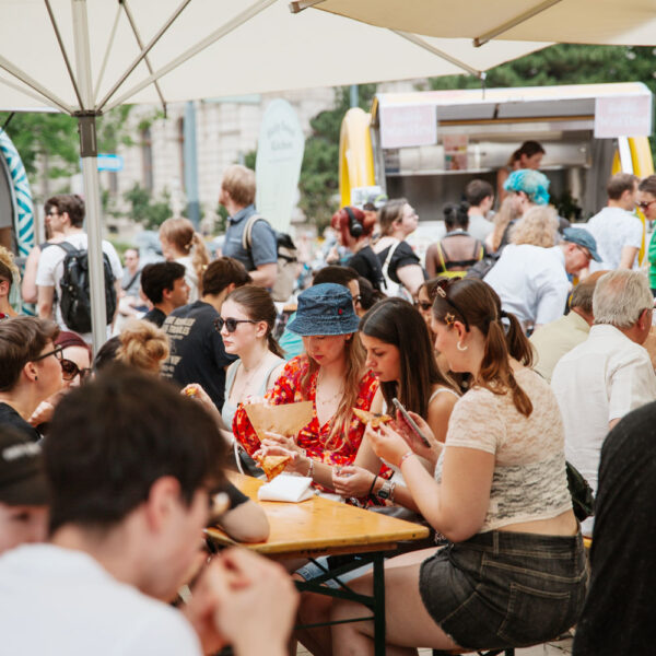 Menschen unter Sonnenschirmen an Tischen essen