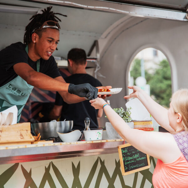 Mann reicht Essen an eine Kundin von einem Foodtruck aus